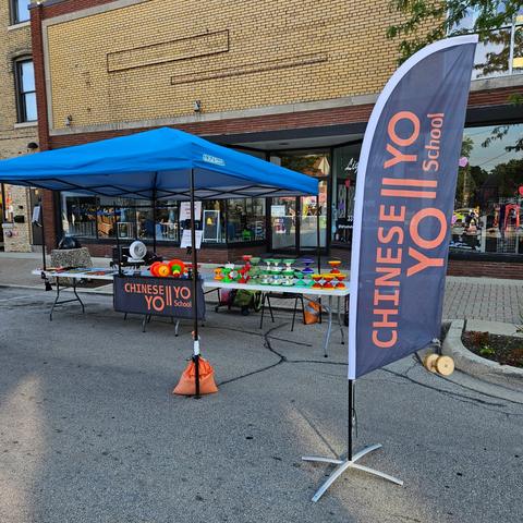 Street booth with blue tent and feather flag in front of shops